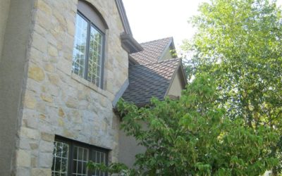 Resource Center 6 Residential home exterior featuring a stone facade, steeply pitched roof, and surrounding greenery, illustrating the importance of roof maintenance and evaluation services offered by Gorilla Exteriors.