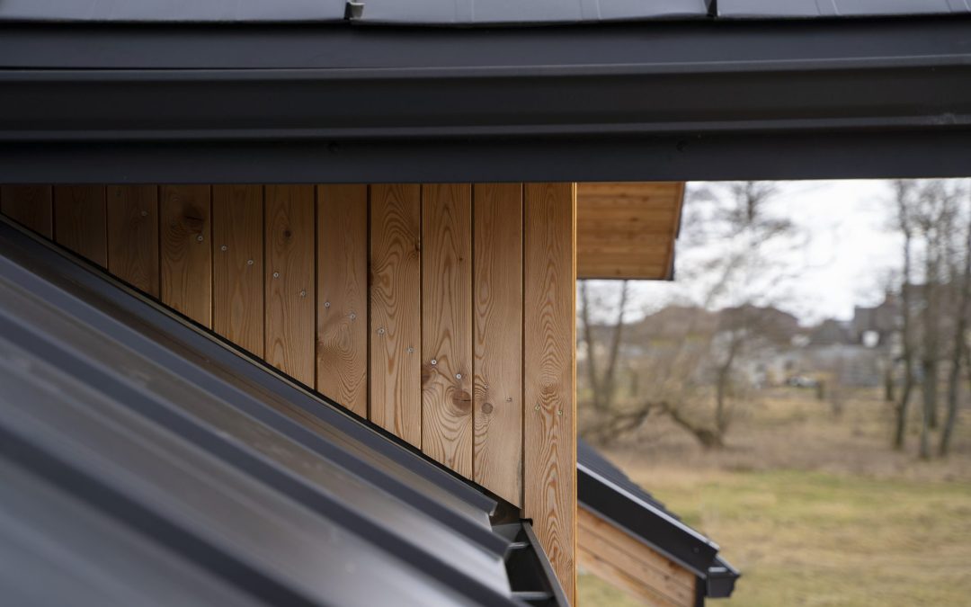 Wooden building structure with a sloped black metal roof and visible wooden siding, emphasizing the importance of proper gutter systems for home protection.